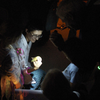 Image of a student holding a snake in a dark room at Museum in the Dark Family Day