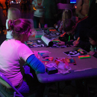 Image of student helping kids with glow-in-the-dark crafts